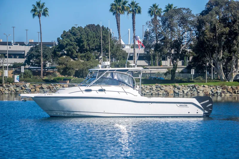 The Image of 2005 Boston Whaler 305 Conquest boat on calm water, surrounded by trees and buildings. - 0
