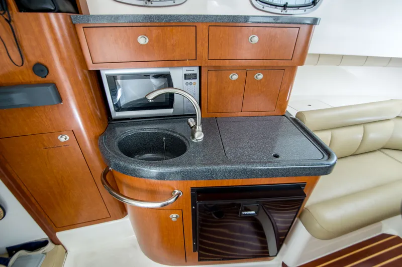 Slide: The Image of 2005 Boston Whaler 305 Conquest interior with kitchenette, featuring sink, microwave, and storage cabinets. - 14