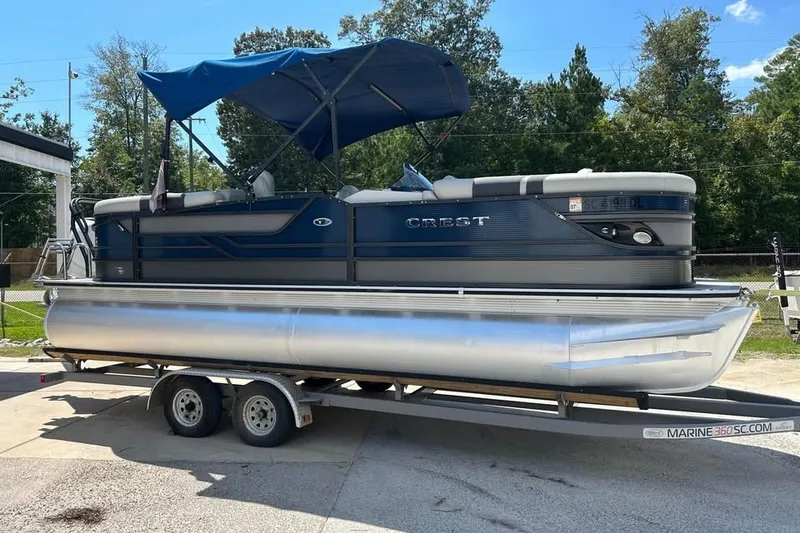 Slide: The Image of 2019 Crest Classic 230 SLC pontoon boat on trailer, blue canopy, parked outdoors. - 11