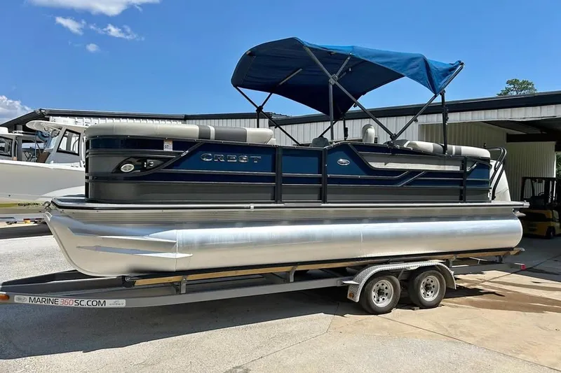 Slide: The Image of 2019 Crest Classic 230 SLC pontoon boat on trailer with blue canopy. - 2