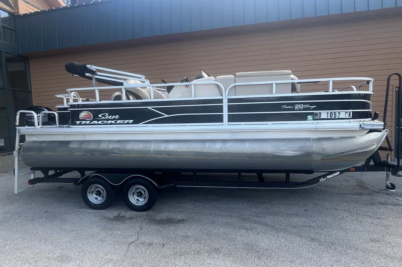 The Image of 2018 Sun Tracker Fishin' Barge 20 DLX pontoon boat on trailer, parked outdoors. - 0
