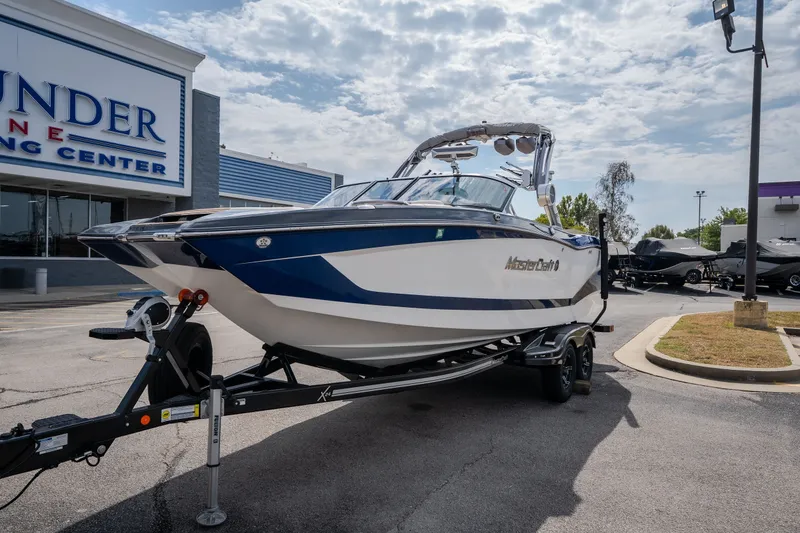Slide: The Image of 2021 MasterCraft X24 boat on trailer at dealership, under cloudy sky. - 3