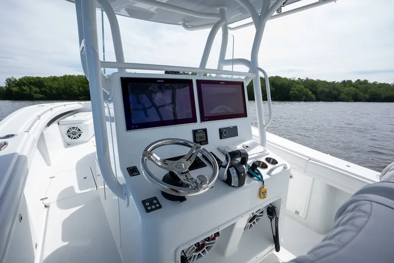 Slide: The Image of 2021 Yellowfin 36 Offshore boat cockpit with dual screens and steering wheel on a calm waterway. - 20