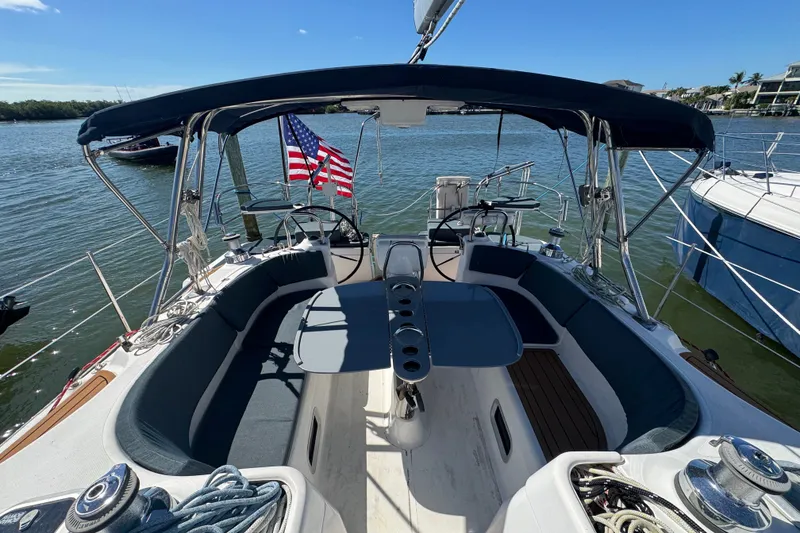 Slide: The Image of 2009 Hunter 49 sailboat cockpit with seating, table, and American flag on calm water. - 108