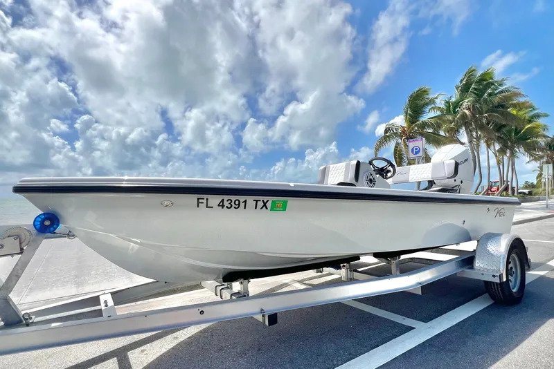 Slide: The Image of 2025 Custom Vtech 18 Flats boat on trailer, parked near palm trees under a cloudy sky. - 16