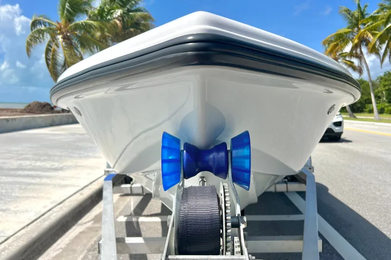 Slide: The Image of Front view of a 2025 Custom Vtech 18 Flats boat on a trailer, with palm trees in the background. - 18