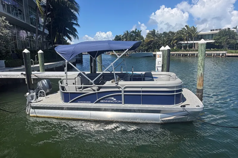 Slide: The Image of 2023 Bennington 20 SVL pontoon boat docked on a sunny waterfront. - 1