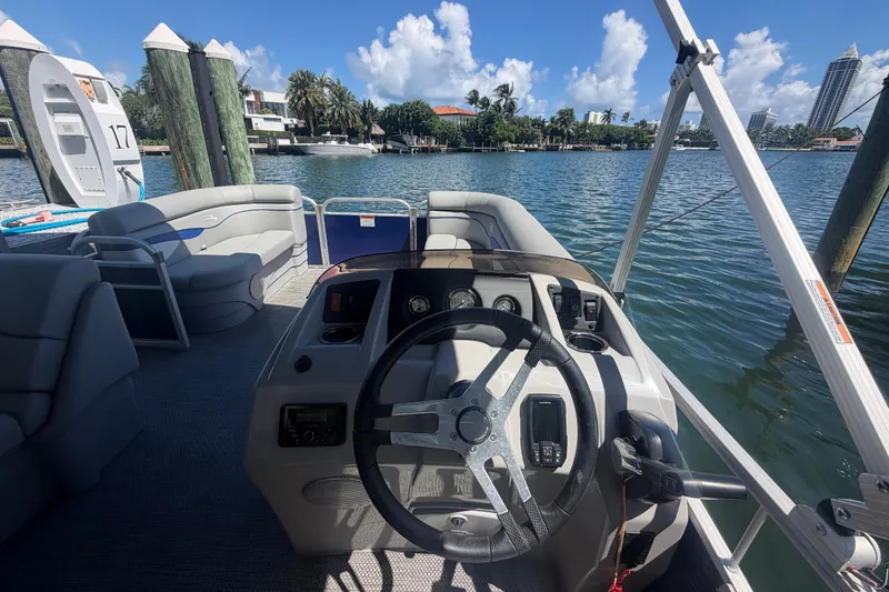 Slide: The Image of 2023 Bennington 20 SVL pontoon boat interior with steering wheel, docked by scenic waterfront. - 7
