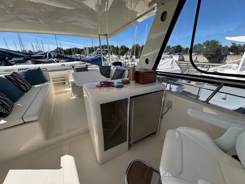 Slide: The Image of The image shows the cockpit of a 1990 Viking 55 Motor Yacht Wide Body. It features comfortable seating, a small table, and a minibar. Other boats are visible in the marina background. - 19