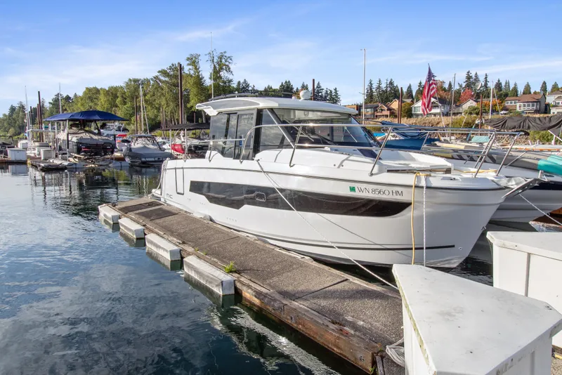 Slide: The Image of 2025 Jeanneau NC 895 Series 2 docked at a marina, surrounded by boats and trees. - 1
