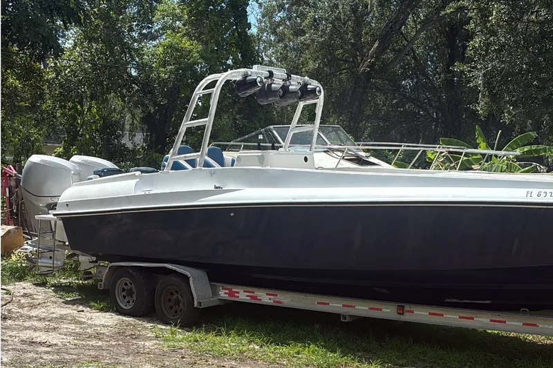 Slide: The Image of Custom Center Console Signature 1990 boat on trailer, surrounded by lush greenery. - 2