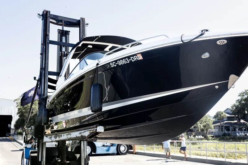 Slide: The Image of 2021 Chaparral 307 SSX boat lifted by forklift, showcasing sleek design and black hull. - 42