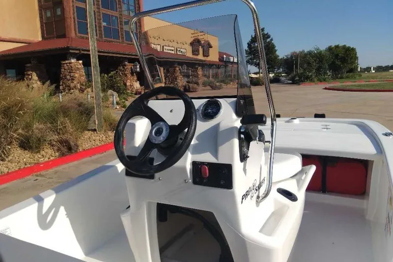 Slide: The Image of 2026 Mako Pro Skiff 13 CC boat with steering console, parked near a building. - 5