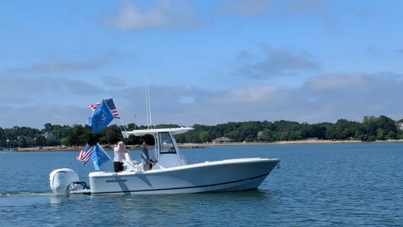 Slide: The Image of A 2025 Regulator 25 boat cruising on calm waters, adorned with several flags. - 4