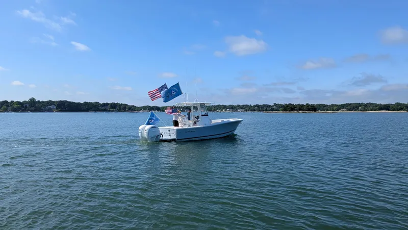Slide: The Image of A 2025 Regulator 25 boat on calm water, flying flags in the wind. - 5