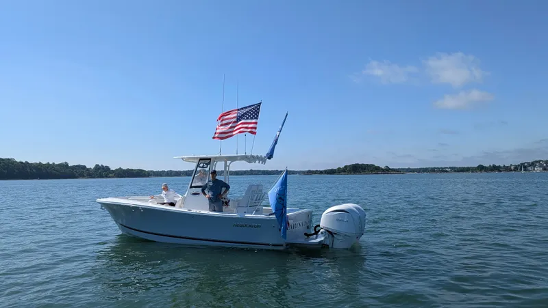 Slide: The Image of A 2025 Regulator 25 boat on calm water with two flags at the stern. - 2
