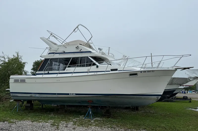 The Image of 1987 Bayliner 3270 Motoryacht on land, white hull, blue trim, parked on stands. - 0