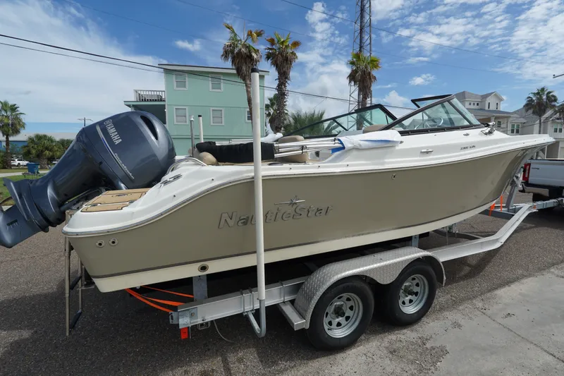 Slide: The Image of 2020 NauticStar 2302 Legacy Dual Console boat on trailer, parked near coastal homes. - 6