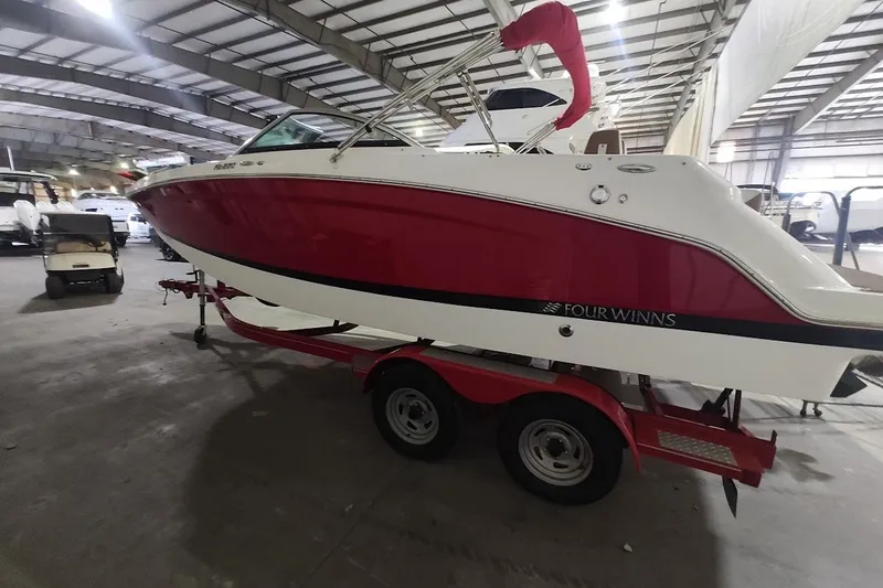 The Image of 2020 Four Winns HD220 boat in a warehouse, red and white design on a trailer. - 0