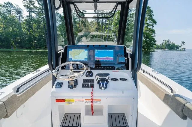Slide: The Image of The image shows the helm of a 2027 Sea Hunt Gamefish 25 boat on a calm lake. - 7