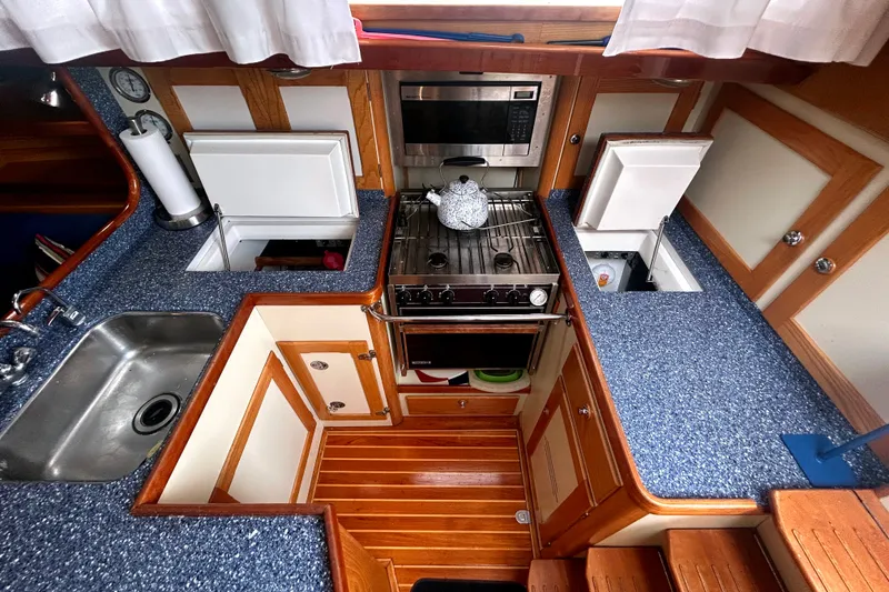 Slide: The Image of Compact yacht kitchen with blue countertops, stainless steel sink, stove, and wooden cabinetry, Alden 43, 1993. - 4