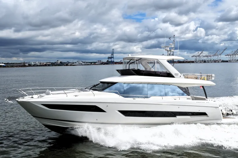 Slide: The Image of 2023 Prestige 690 yacht cruising on a cloudy day near industrial port. - 14