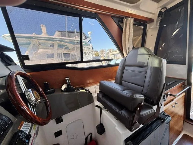 Slide: The Image of Interior view of a boat with a cushioned captain's chair, wooden steering wheel, and large windows. - 31