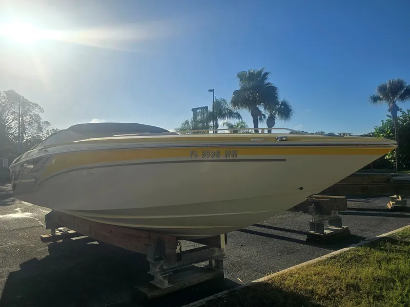 Slide: The Image of A yellow 2007 Baja 26 Outlaw boat sits on a trailer under palm trees in sunlight. - 2