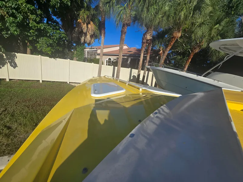 Slide: The Image of A yellow boat parked next to a white fence and palm trees. Another boat is visible beside it. - 13