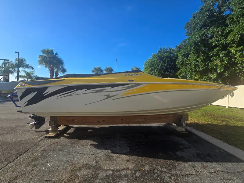 The Image of A yellow 2007 Baja 26 Outlaw boat on a wooden stand, surrounded by palm trees. - 0