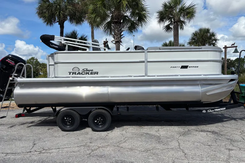 The Image of 2027 Sun Tracker Party Barge 20 DLX pontoon boat on trailer, parked under palm trees. - 0