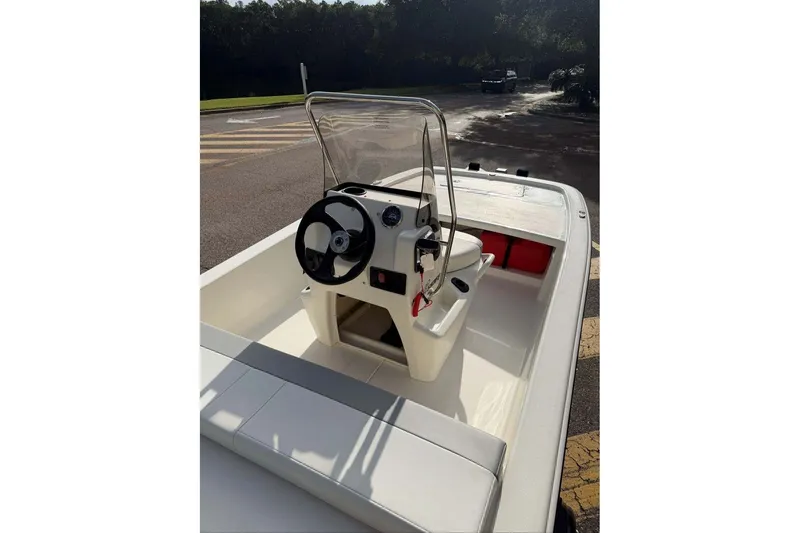 Slide: The Image of 2026 Mako Pro Skiff 13 CC boat with steering console and seating, parked outdoors. - 7