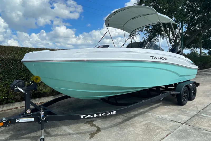 Slide: The Image of 2027 Tahoe T21 boat on trailer, light blue hull, parked outdoors under cloudy sky. - 2