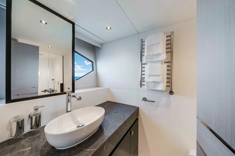 Slide: The Image of The image shows a modern bathroom on a Sunseeker Manhattan 68 yacht. It features a sleek sink, mirror, and towel rack. - 40