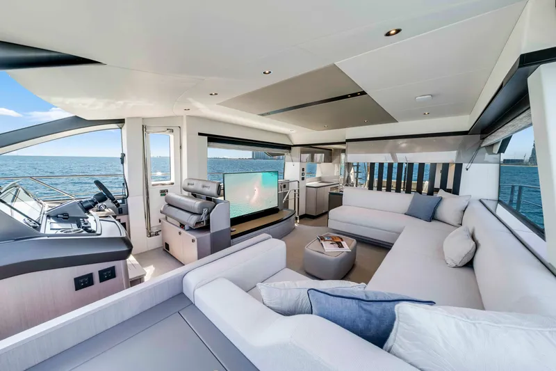 Slide: The Image of The image shows the luxurious interior of a Sunseeker Manhattan 68 yacht. There's a spacious seating area with white sofas and blue cushions. A large TV is visible, and the sea can be seen through the windows. - 23