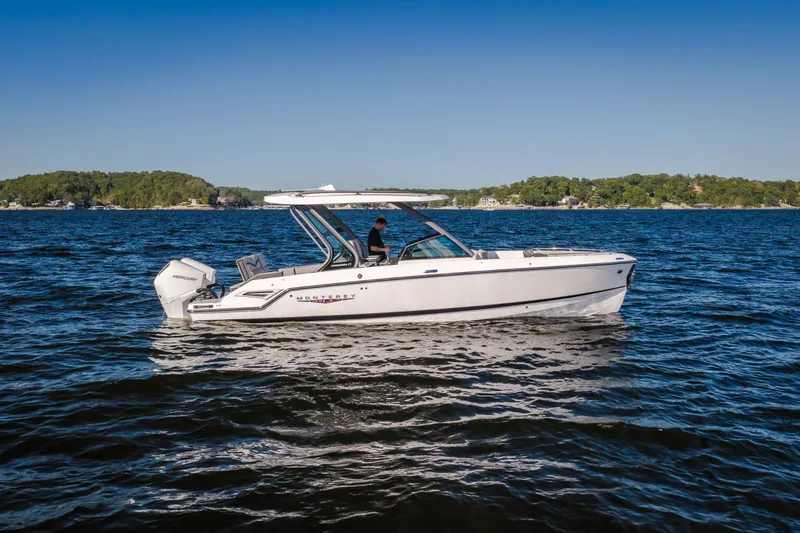 The Image of 2027 Monterey Elite 27 OB boat cruising on a serene lake under a clear blue sky. - 1