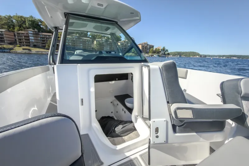 Slide: The Image of 2027 Monterey Elite 27 OB boat interior with seating and cabin, on a scenic lake. - 64
