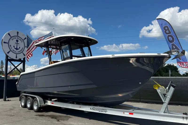 The Image of 2025 Robalo R302 Center Console boat on trailer, displayed outdoors with flags. - 0