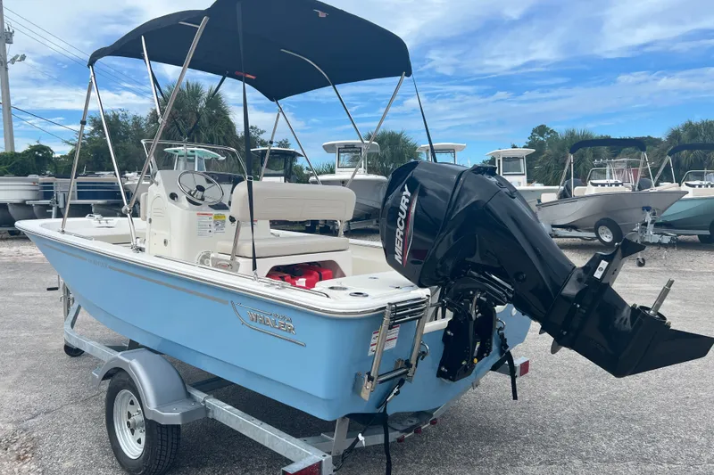 Slide: The Image of 2027 Boston Whaler 150 Montauk boat with Mercury engine on trailer, under blue sky. - 6