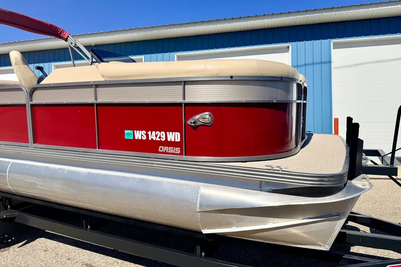 Slide: The Image of 2021 Manitou 23 Oasis pontoon boat with red exterior, parked on a trailer. - 102