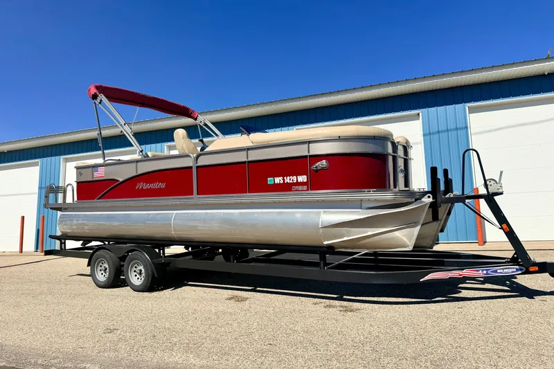 The Image of 2021 Manitou 23 Oasis pontoon boat on trailer, parked outside blue building. - 0