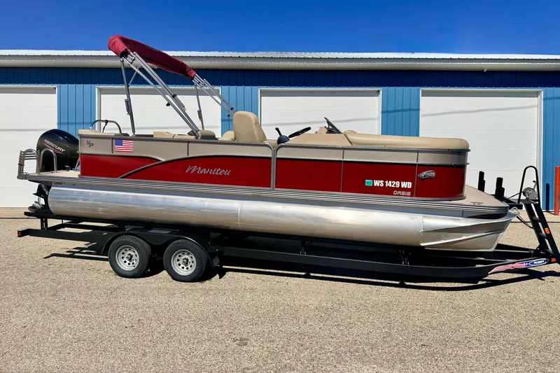 Slide: The Image of 2021 Manitou 23 Oasis pontoon boat with red and beige design on a trailer. - 4