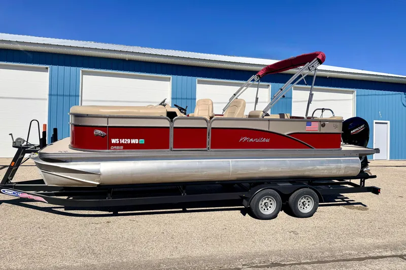 Slide: The Image of 2021 Manitou 23 Oasis pontoon boat on trailer, red and beige design, parked outdoors. - 107