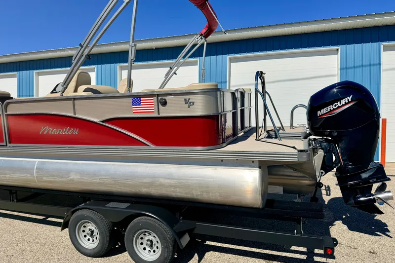 Slide: The Image of 2021 Manitou 23 Oasis pontoon boat with Mercury engine on trailer, blue building background. - 111
