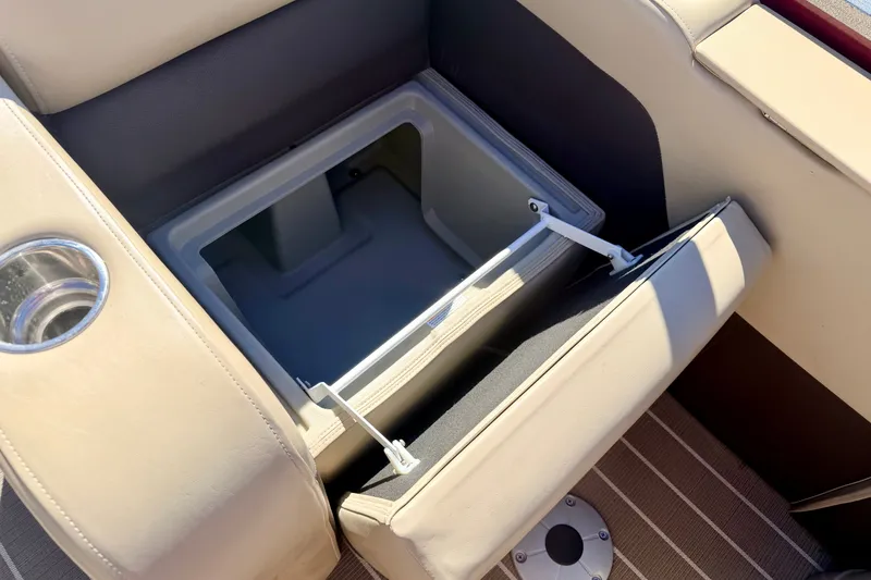 Slide: The Image of Open storage compartment in 2021 Manitou 23 Oasis boat with beige seating and cup holder. - 34