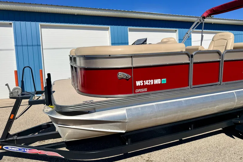 Slide: The Image of 2021 Manitou 23 Oasis pontoon boat with red exterior, parked on a trailer. - 7