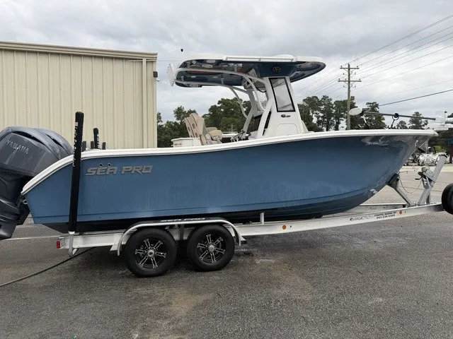 The Image of A 2024 Sea Pro 262 Center Console boat on a trailer, featuring a blue hull and twin outboard engines. - 0