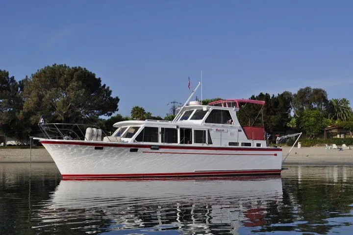 The Image of 1983 Roughwater 41 boat on calm water near a sandy beach and trees. - 1