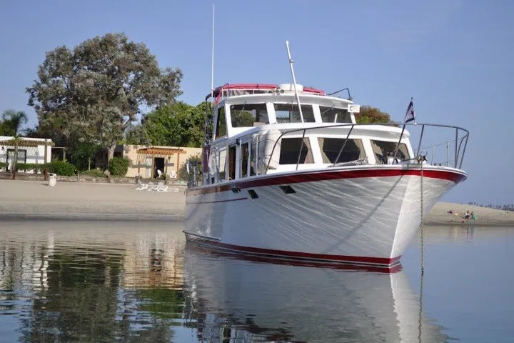Slide: The Image of 1983 Roughwater 41 boat anchored near a sandy beach with trees in the background. - 44