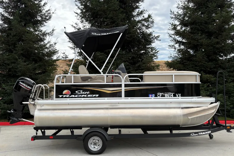 The Image of 2025 Sun Tracker Party Barge 16 DLX pontoon boat on trailer, parked outdoors. - 0